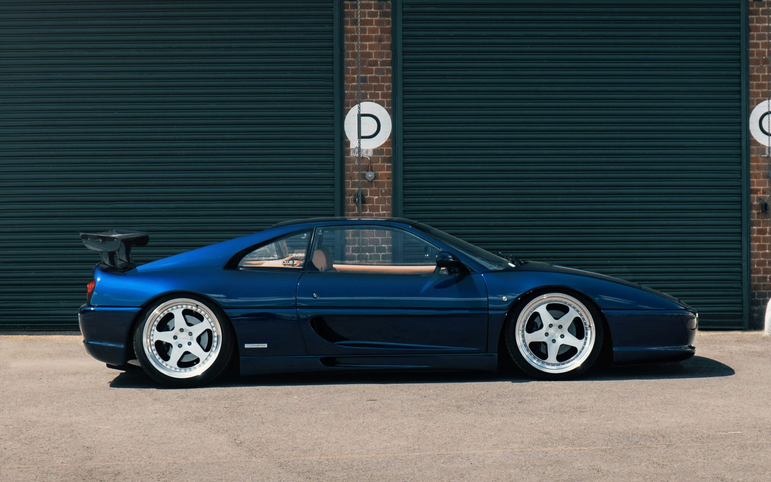 A side-profile shot of a dark blue modified Ferrari F355.