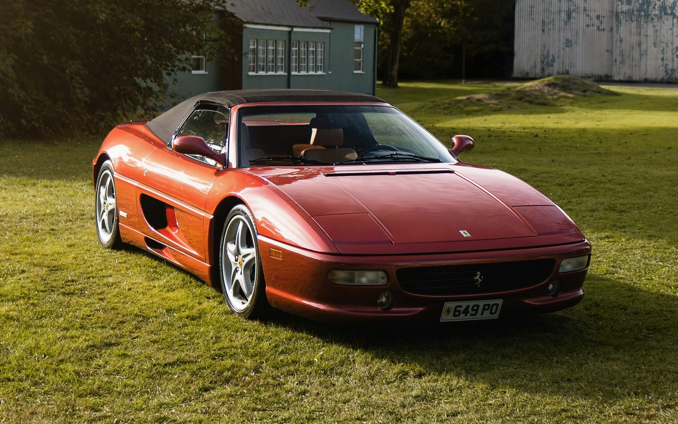A dark red Ferrari F355 Spider parked on a lawn.