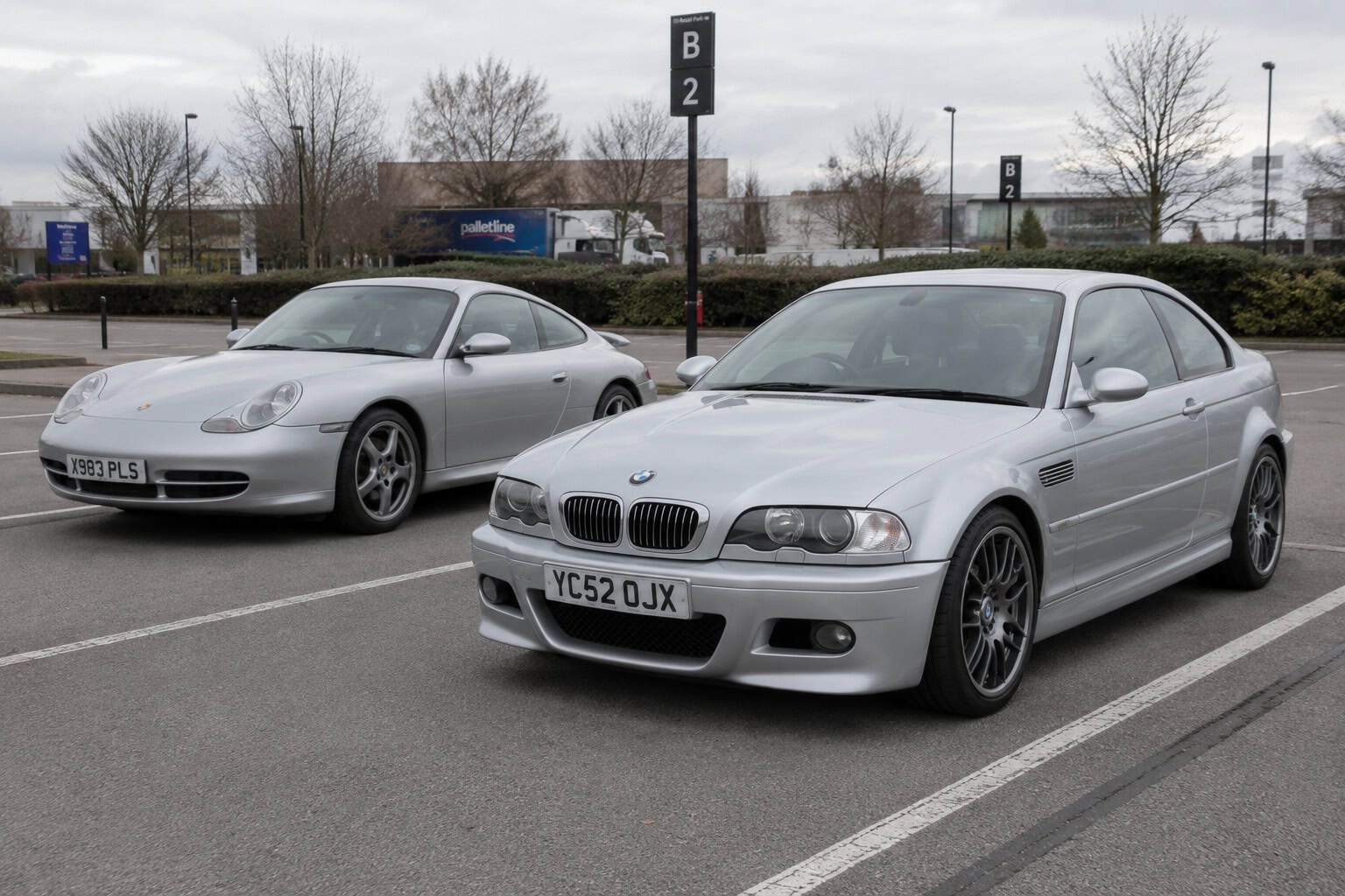 A BMW E46 M3 and a Porsche 996 911 parked on a public car park.