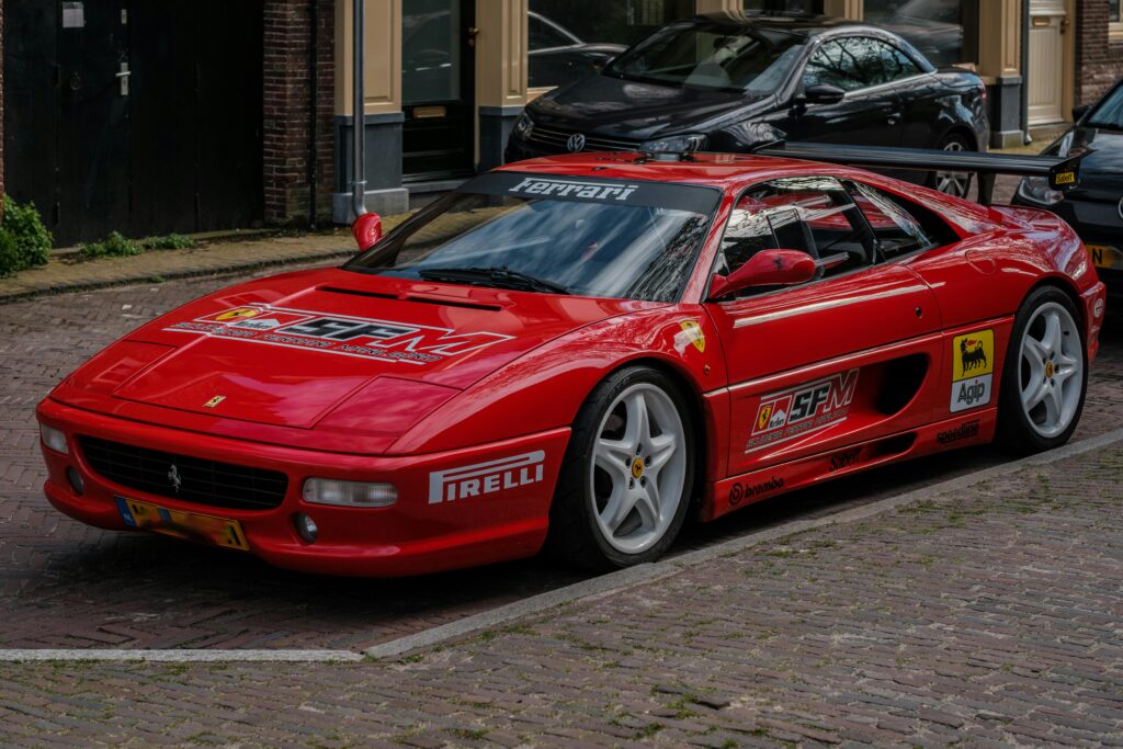 A red modified Ferrari F355 with stickers parked on the street.