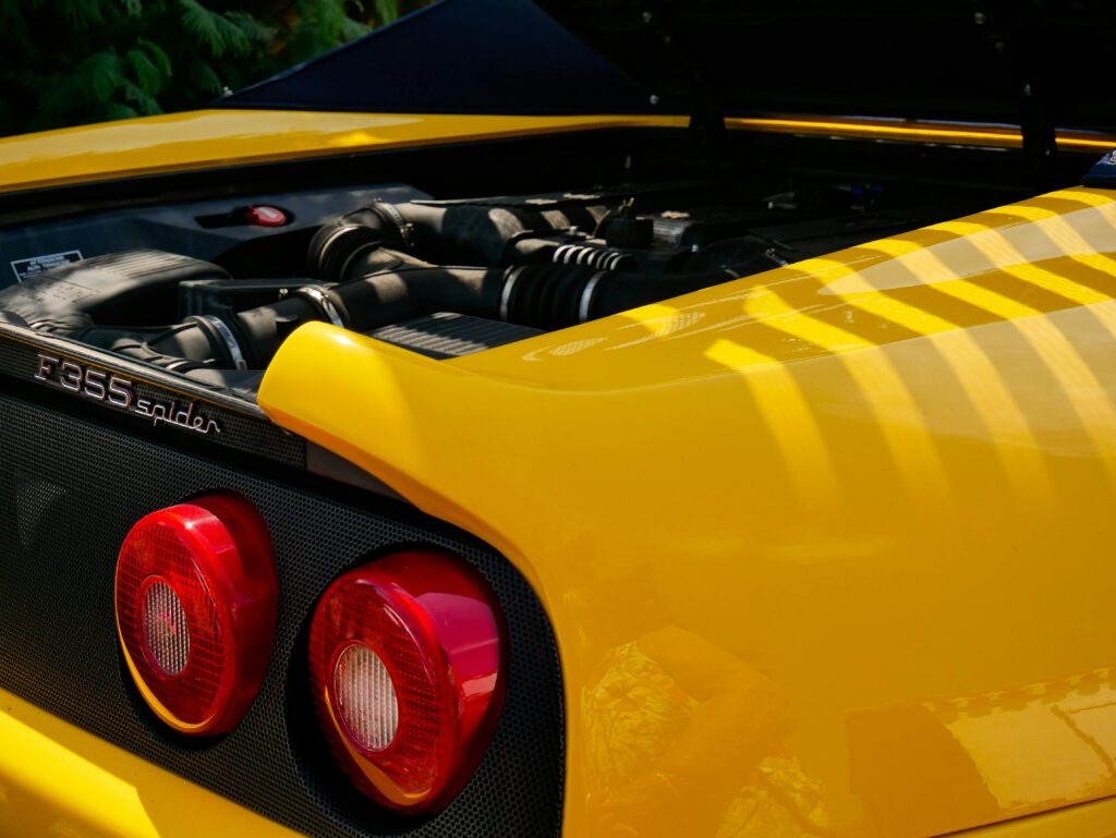 A close-up of a yellow Ferrari F355 Spider badge and rear light.