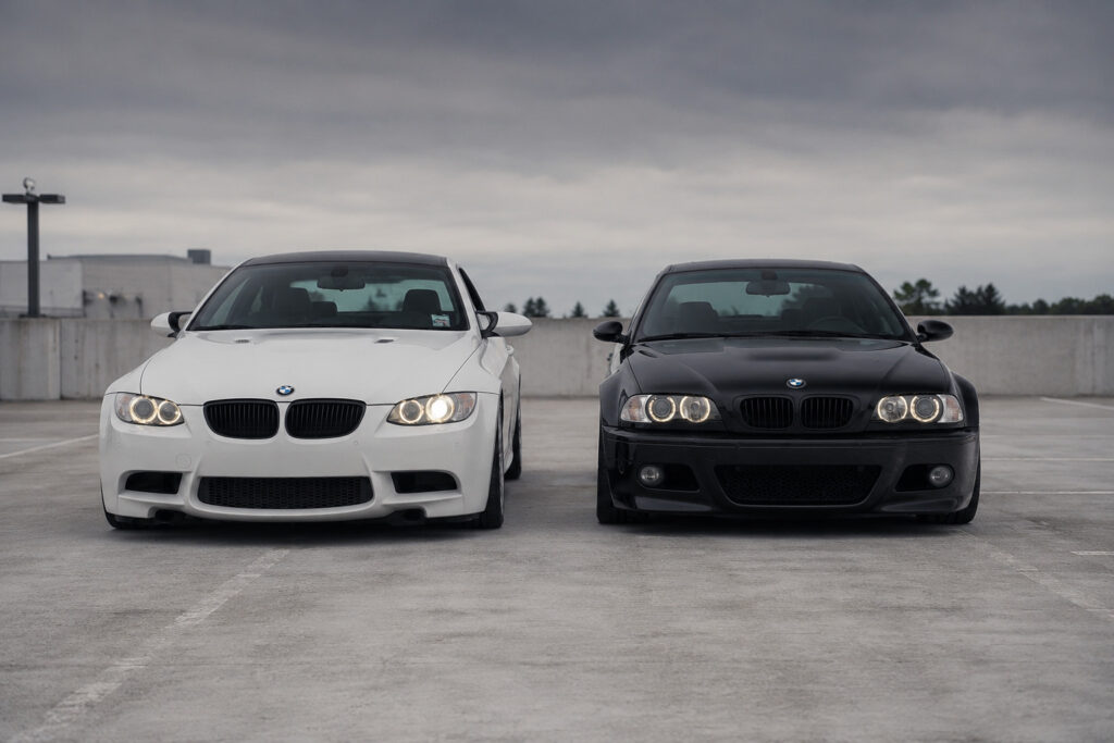 BMW E46 M3 vs BMW E92 M3 parked next to each other on a rooftop parking lot.