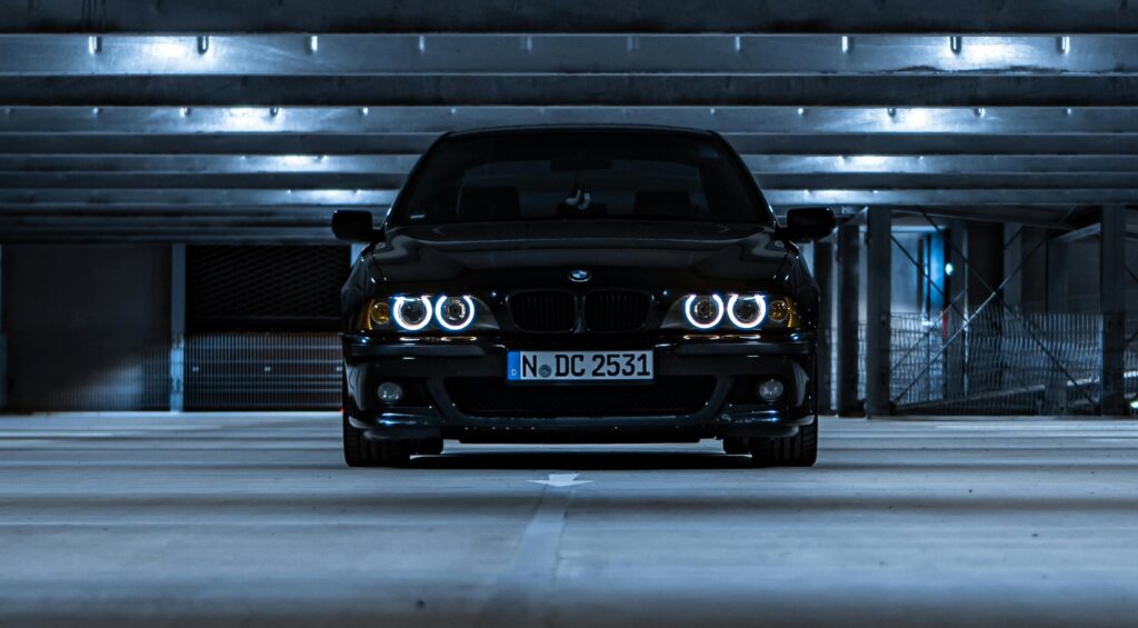 A front-end view of a black E39 BMW M5 in a dark garage.