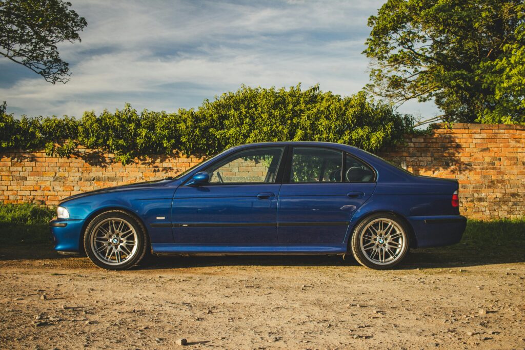 A side profile view of a blue BMW E39 M5 parked in a rural setting.