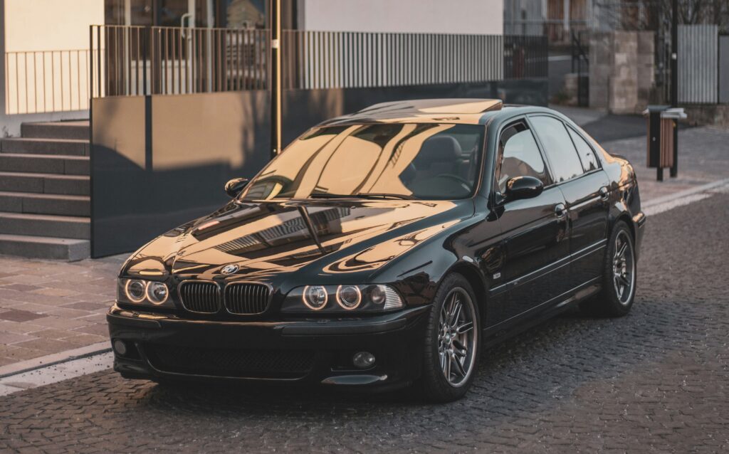 A black E39 BMW M5 parked on a cobbled street.