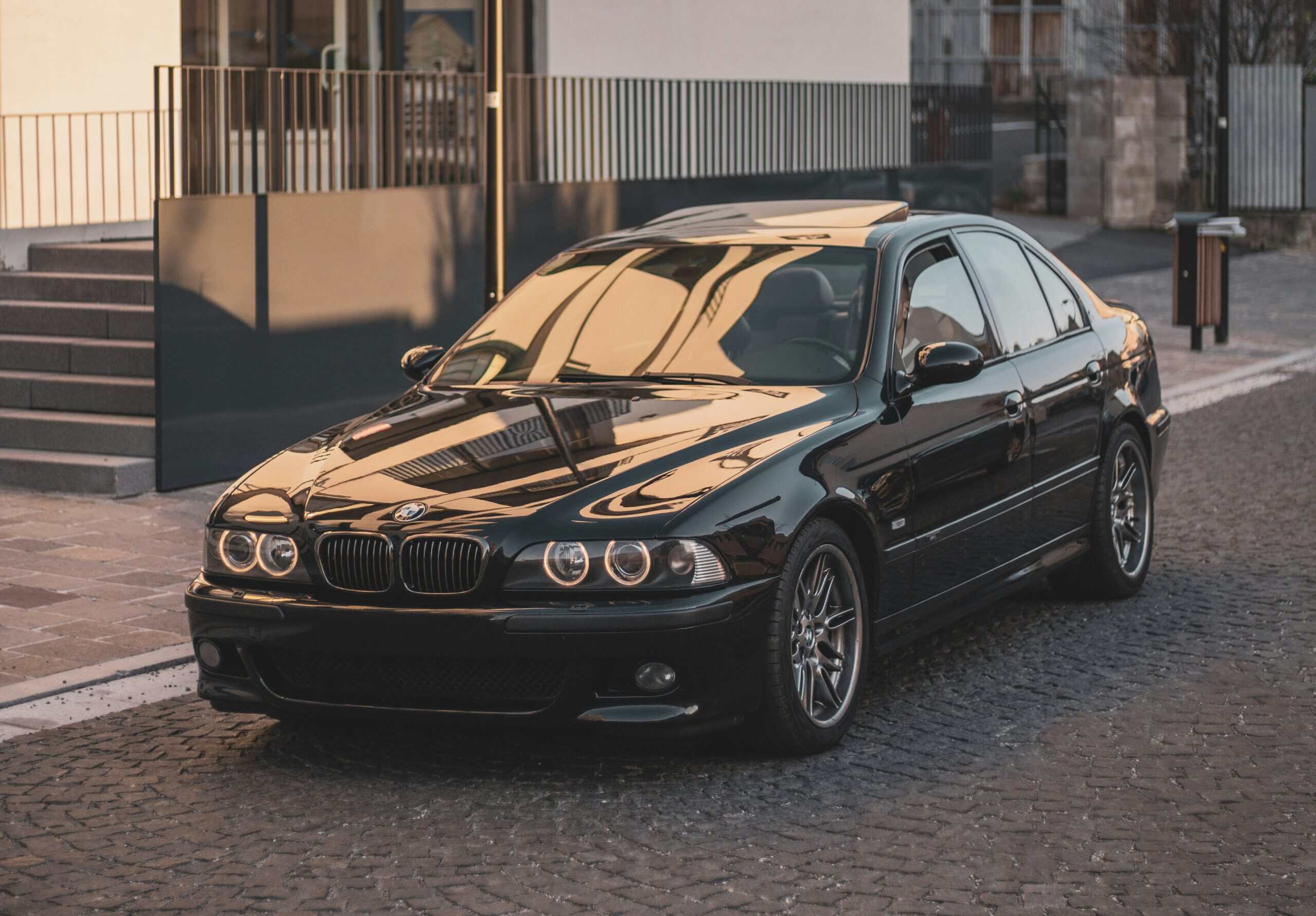 Black BMW sedan parked on cobblestone street in urban setting.