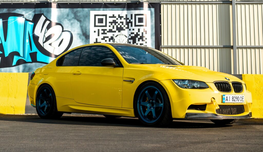 A yellow BMW E92 M3 coupe parked in front of a wall.