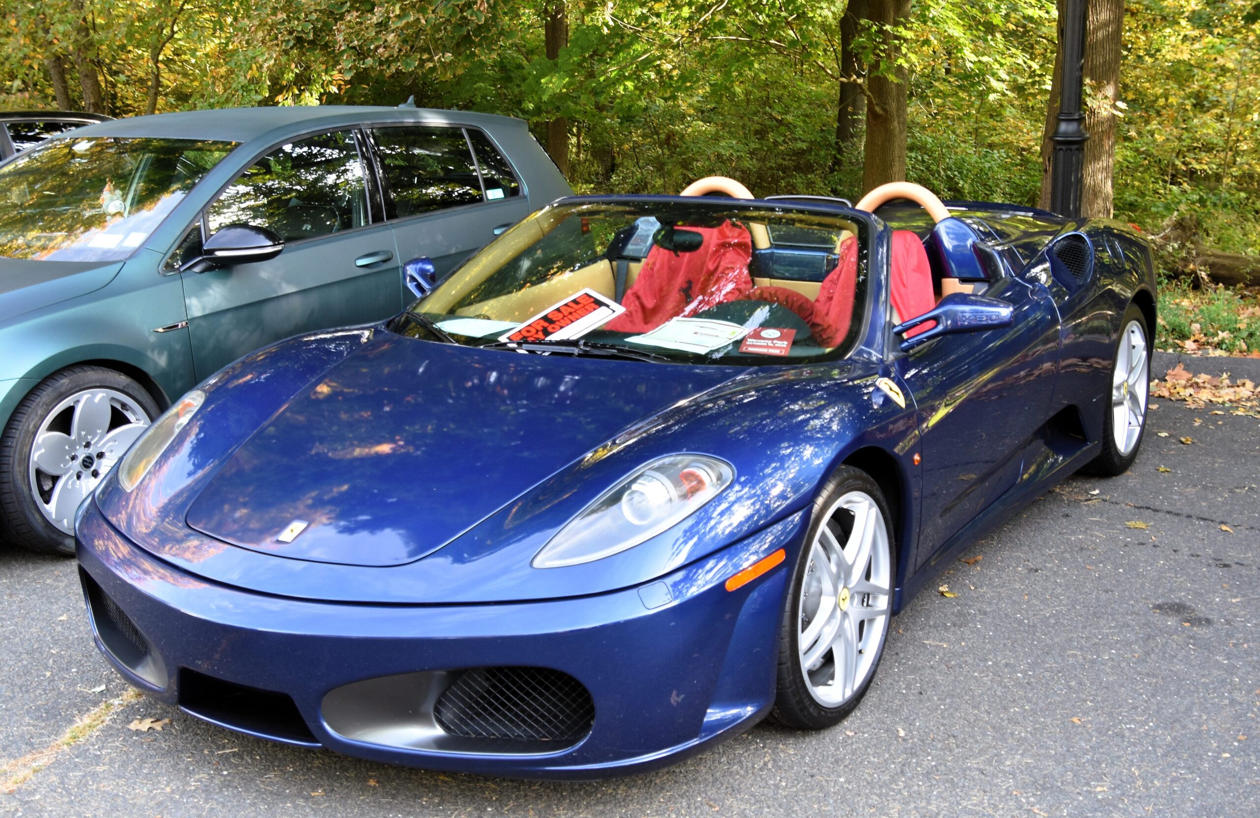 A blue Ferrari F430 Spyder with a red interior parked outside.